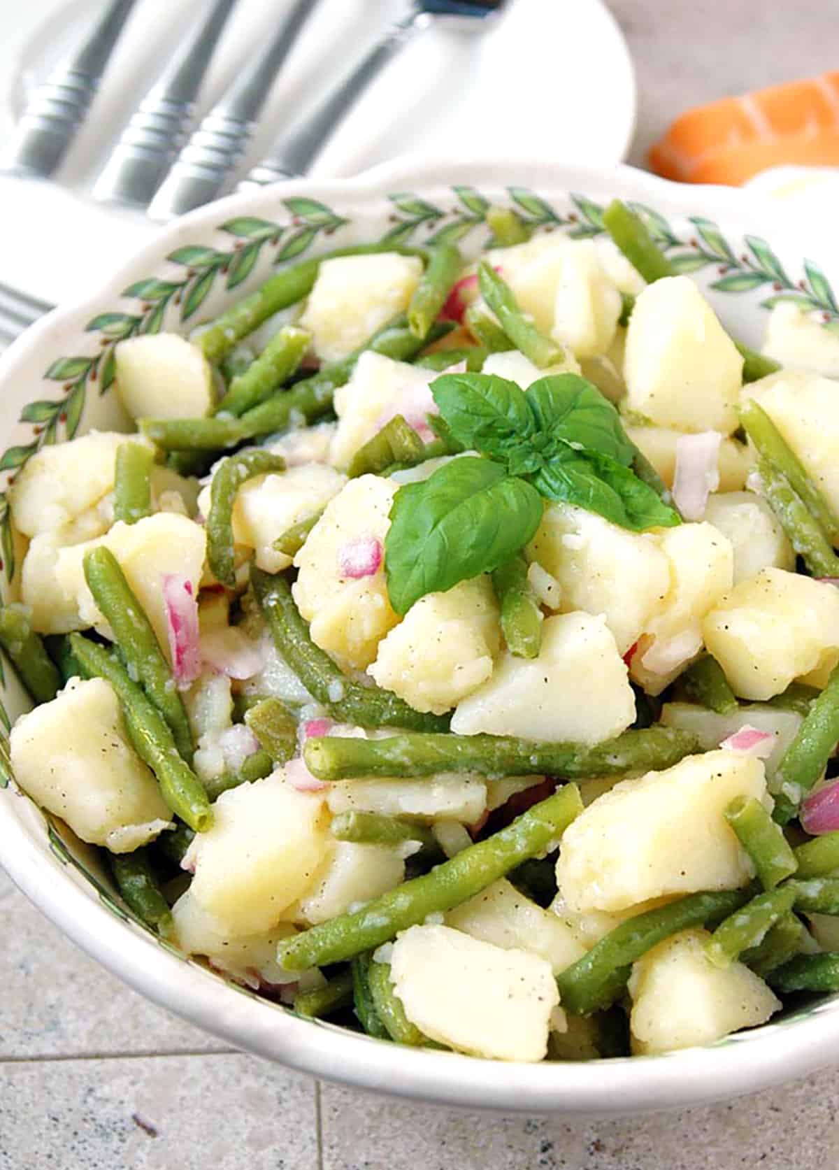 prepared italian potato salad with green beans in a bowl with basil on top