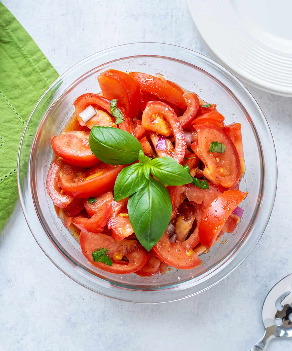 Prepared tomato salad in a glass bowl with basil on top.