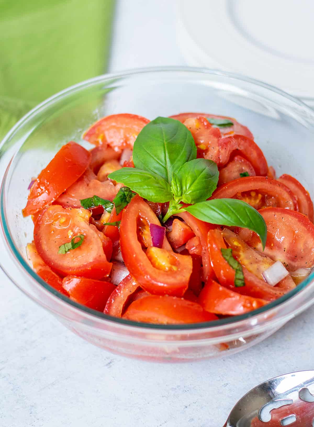 Prepared tomato salad in a glass bowl with basil on top.