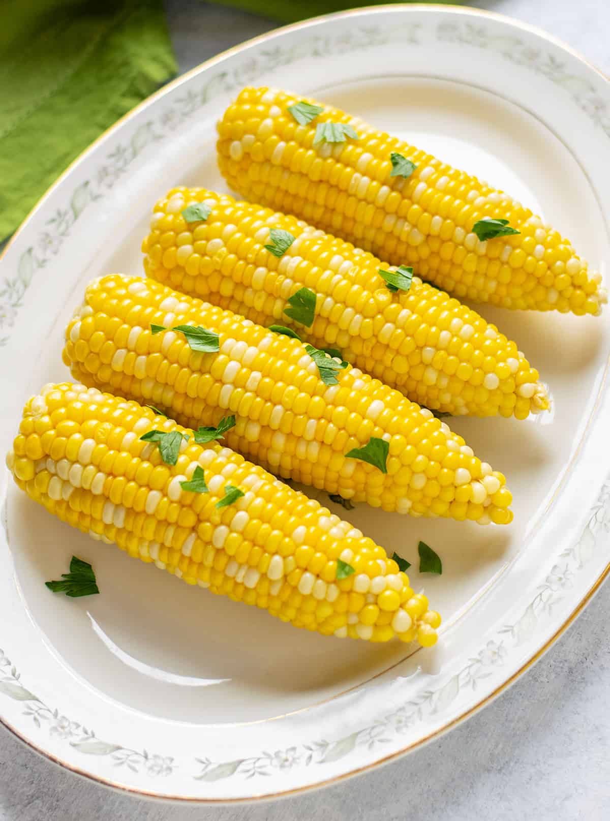 four ears of corn on the cob on a platter with parsley