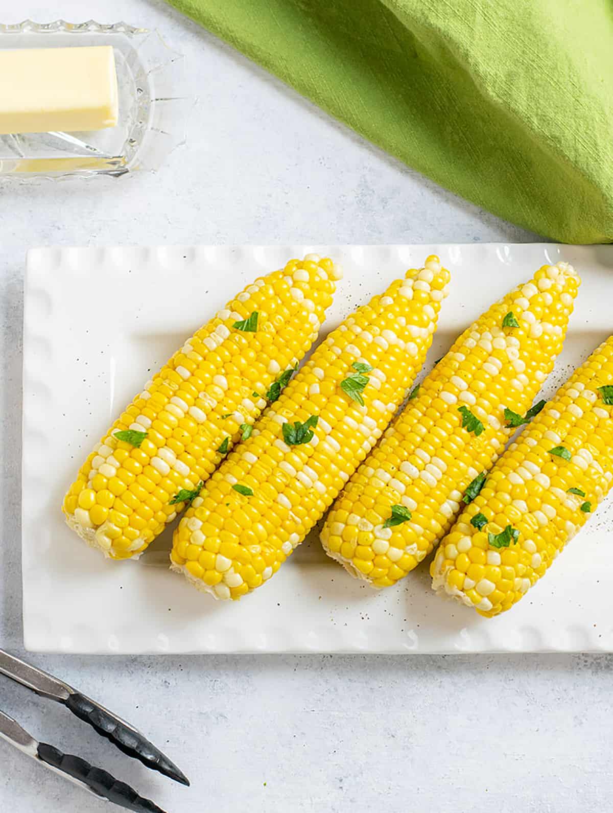 four ears of corn on the cob on a platter with parsley