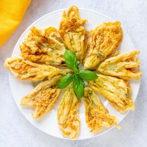 fried zucchini flowers arranged on a plate with basil on top