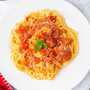 plate of spaghetti topped with sauce and cheese. garnished with basil.