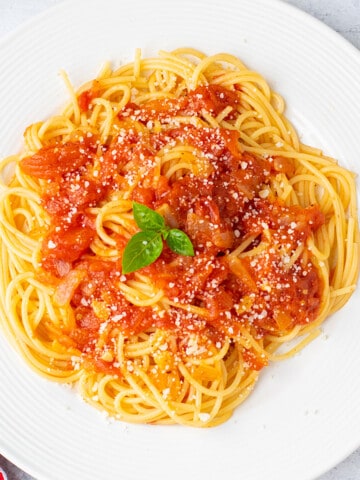 plate of spaghetti topped with sauce and cheese. garnished with basil.