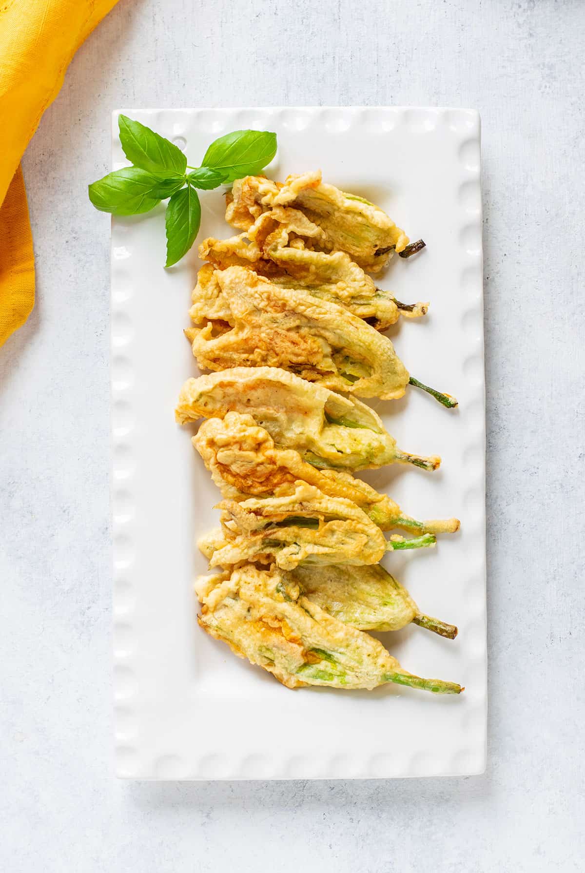 platter of fried zucchini flowers with basil on the side.