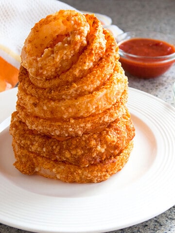 tower of onion rings with dipping sauces in the background.