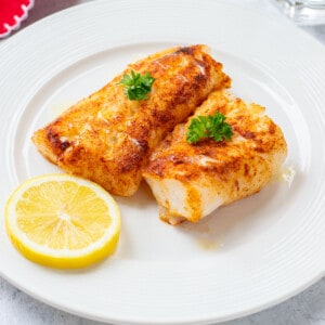 two grilled cod loins on plate with lemon and melted butter.