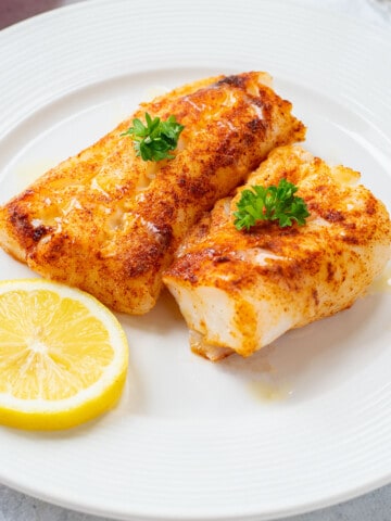 two grilled cod loins on plate with lemon and melted butter.