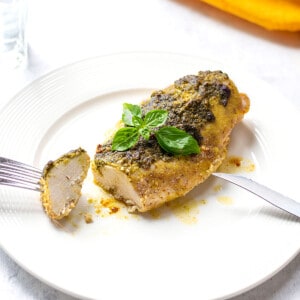 chicken breast with pesto on a plate with forkful of chicken and knife.