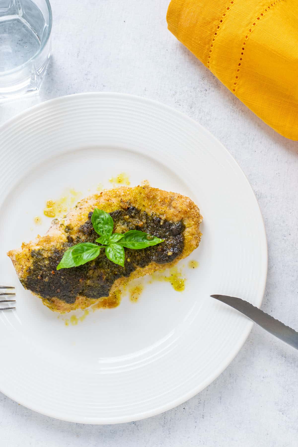 cooked pesto chicken breast on plate with basil, fork and knife.