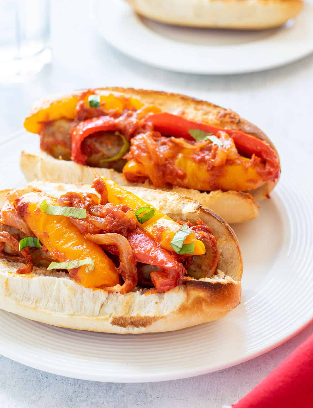 two sausage and pepper sandwiches on a plate topped with sauce and basil