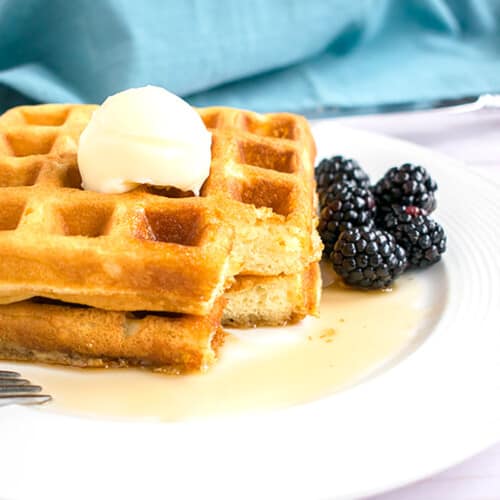 stack of homemade waffles with butter, syrup and blackberries
