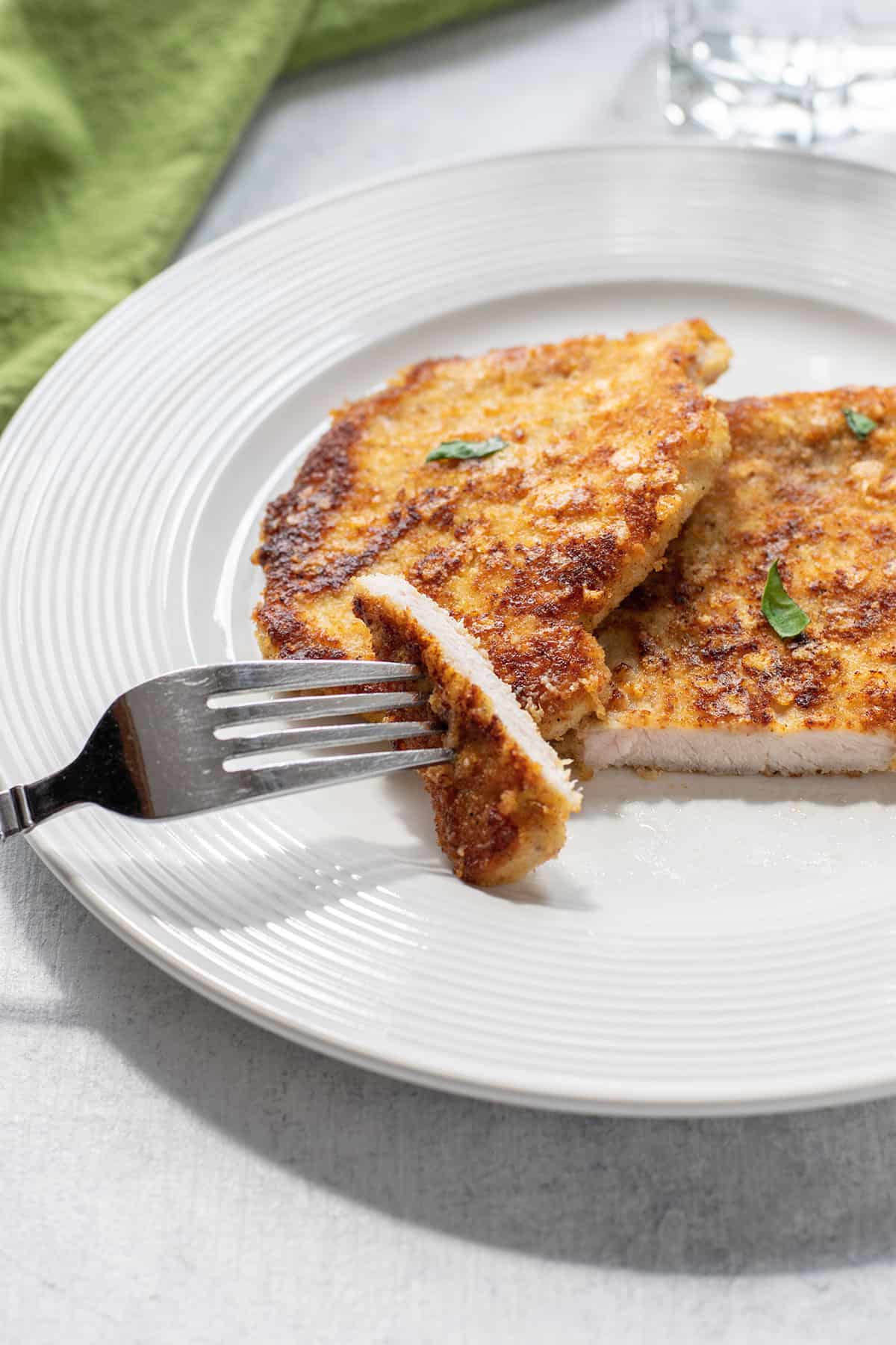 breaded pork chops on a plate cut open with a fork.