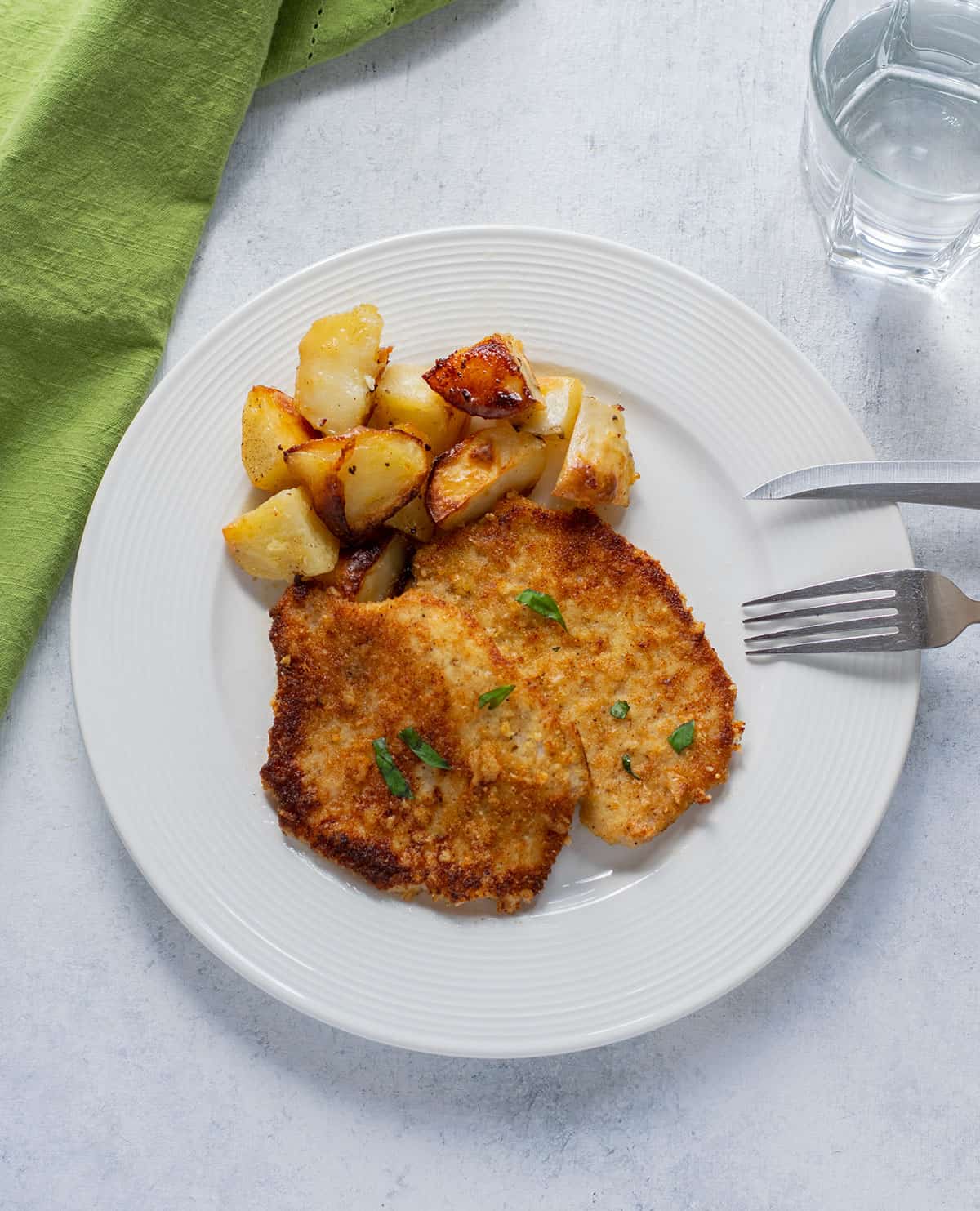 breaded pork chops on a plate with roasted potatoes.