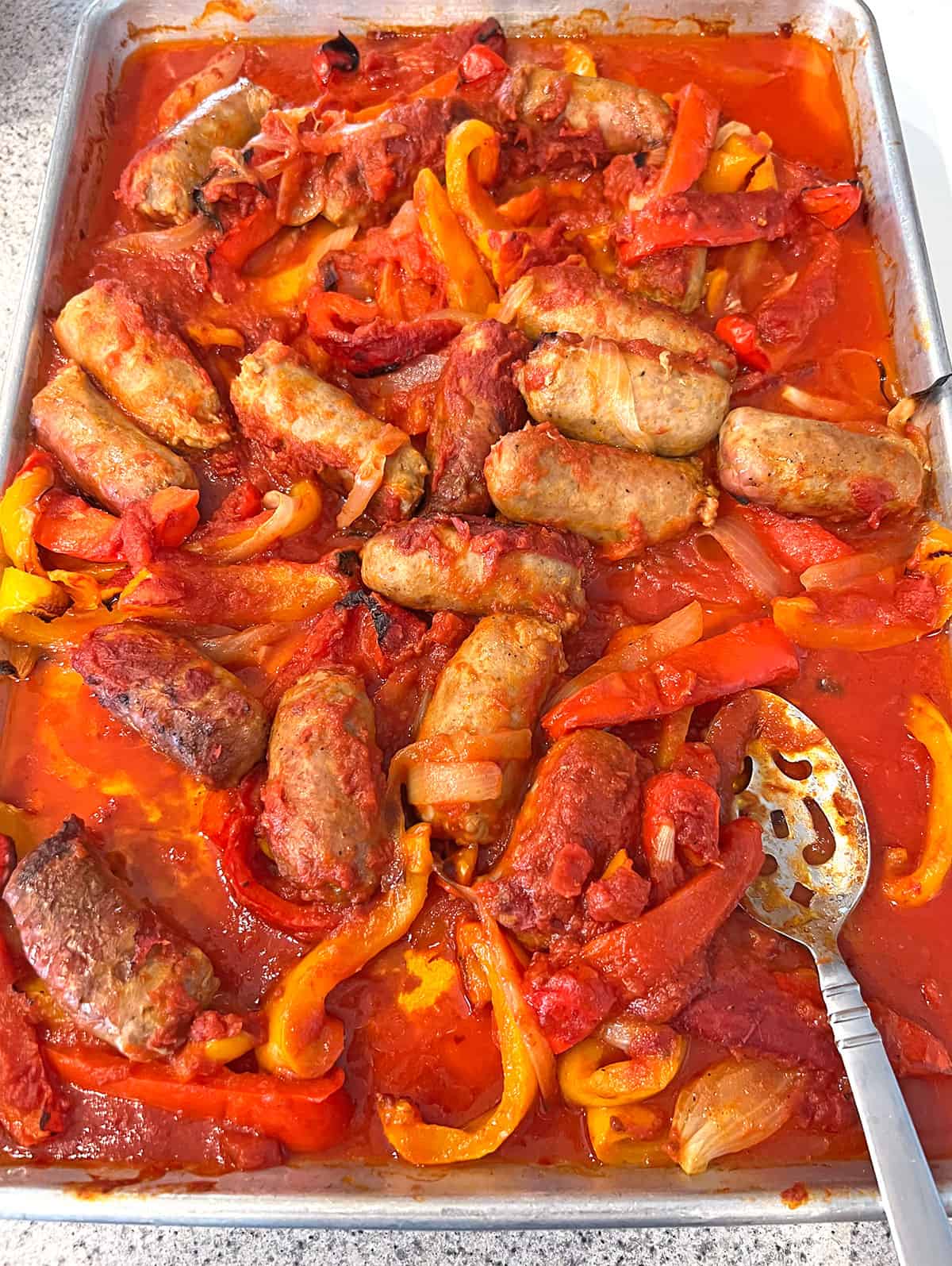 sheet pan with roasted Italian sausage, peppers and onions in tomato sauce.