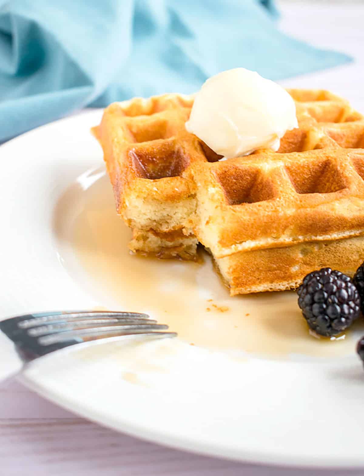 prepared waffle on a plate with butter, syrup and blackberries