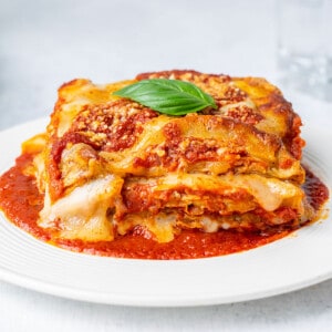 portion of eggplant Parmesan on white plate with tomato sauce and basil.