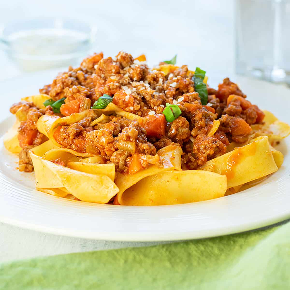 plate of beef bolognese over pasta garnished with basil