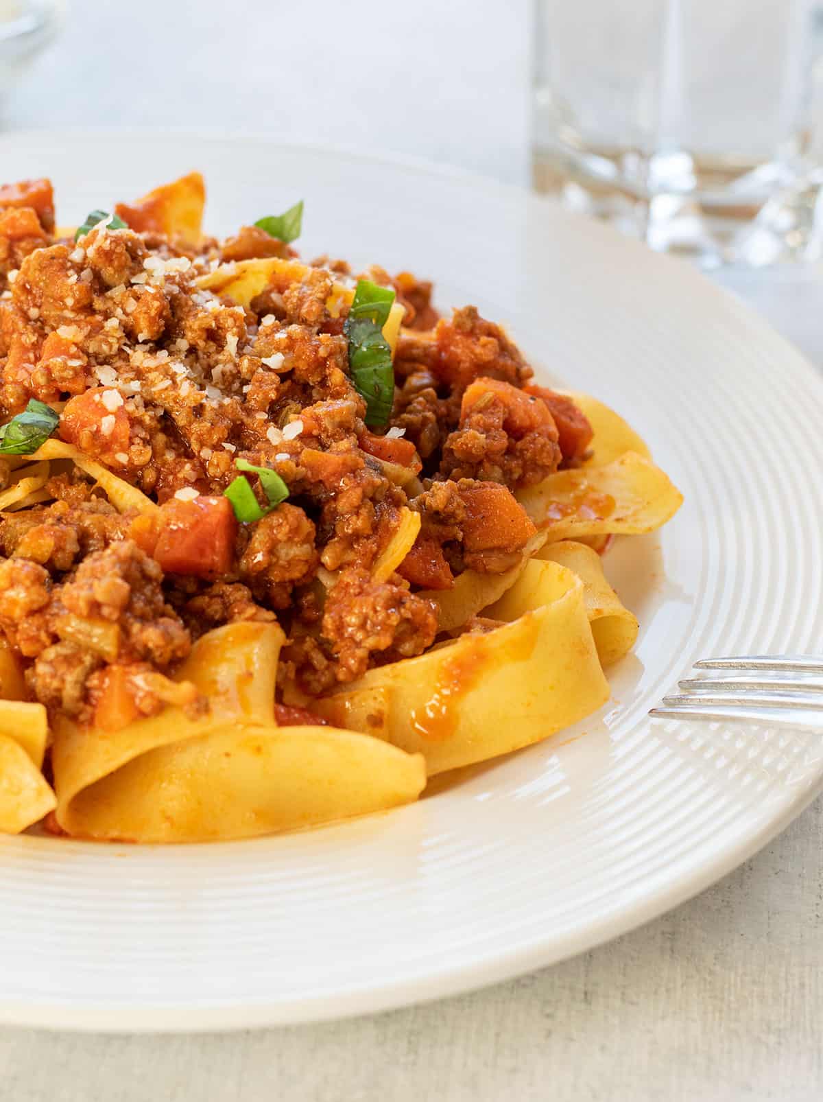 plate of beef bolognese over pasta garnished with basil