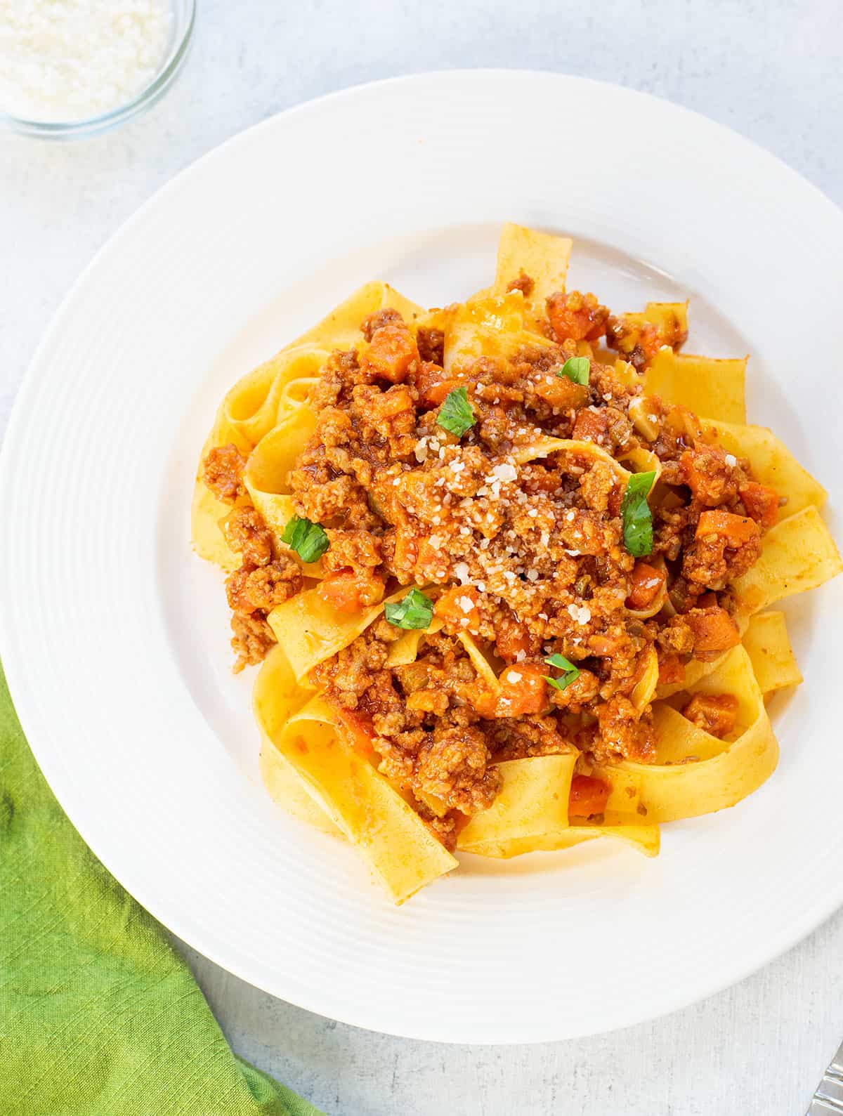 plate of beef bolognese over pasta garnished with basil