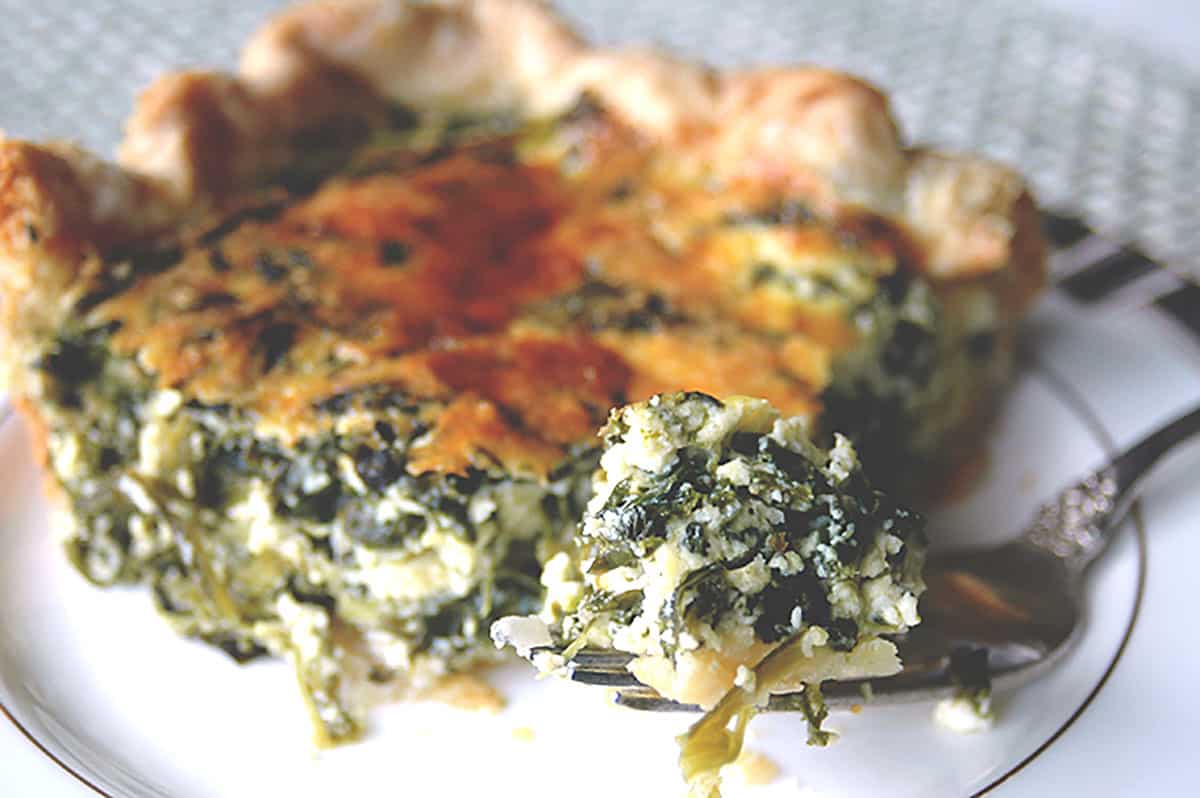 fork-full of spinach ricotta pie with a slice on a plate
