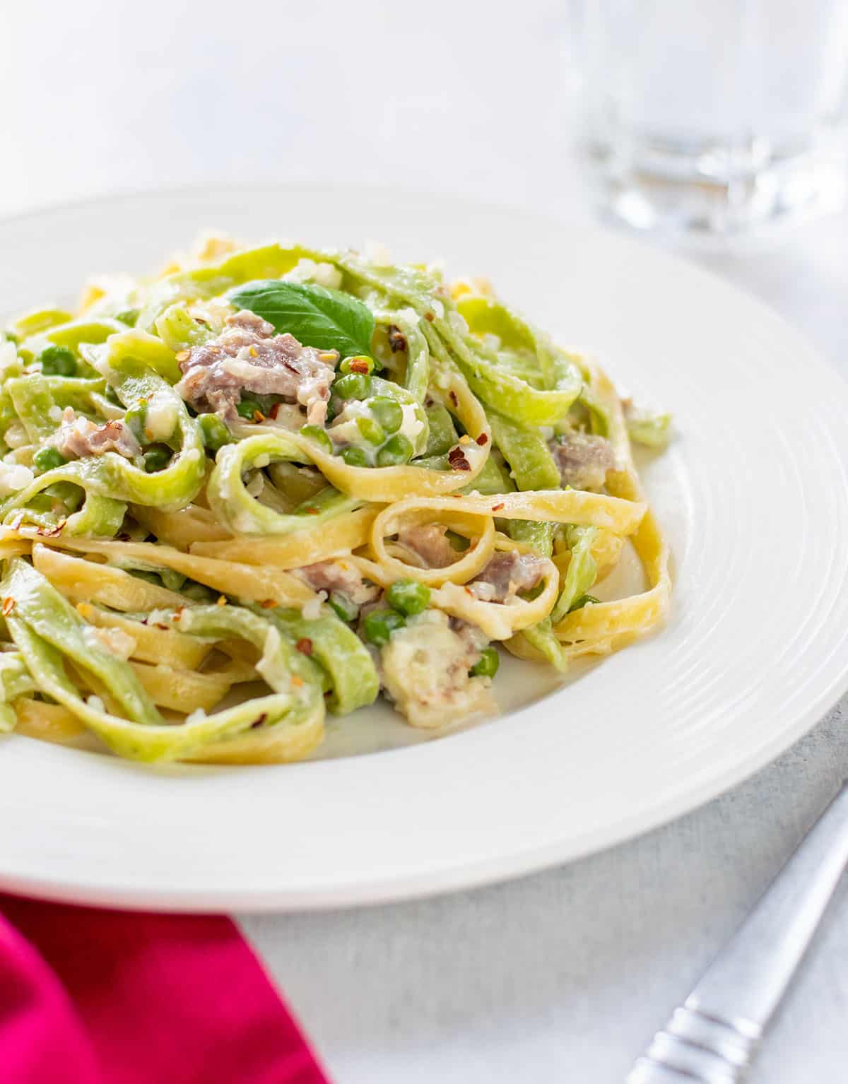 plate of straw and hay pasta garnished with a basil leaf.