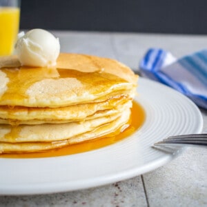 stack of pancakes with butter and syrup on white plate with fork