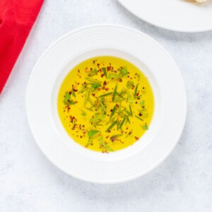 bowl of dipping oil with fresh herbs and pepper flakes