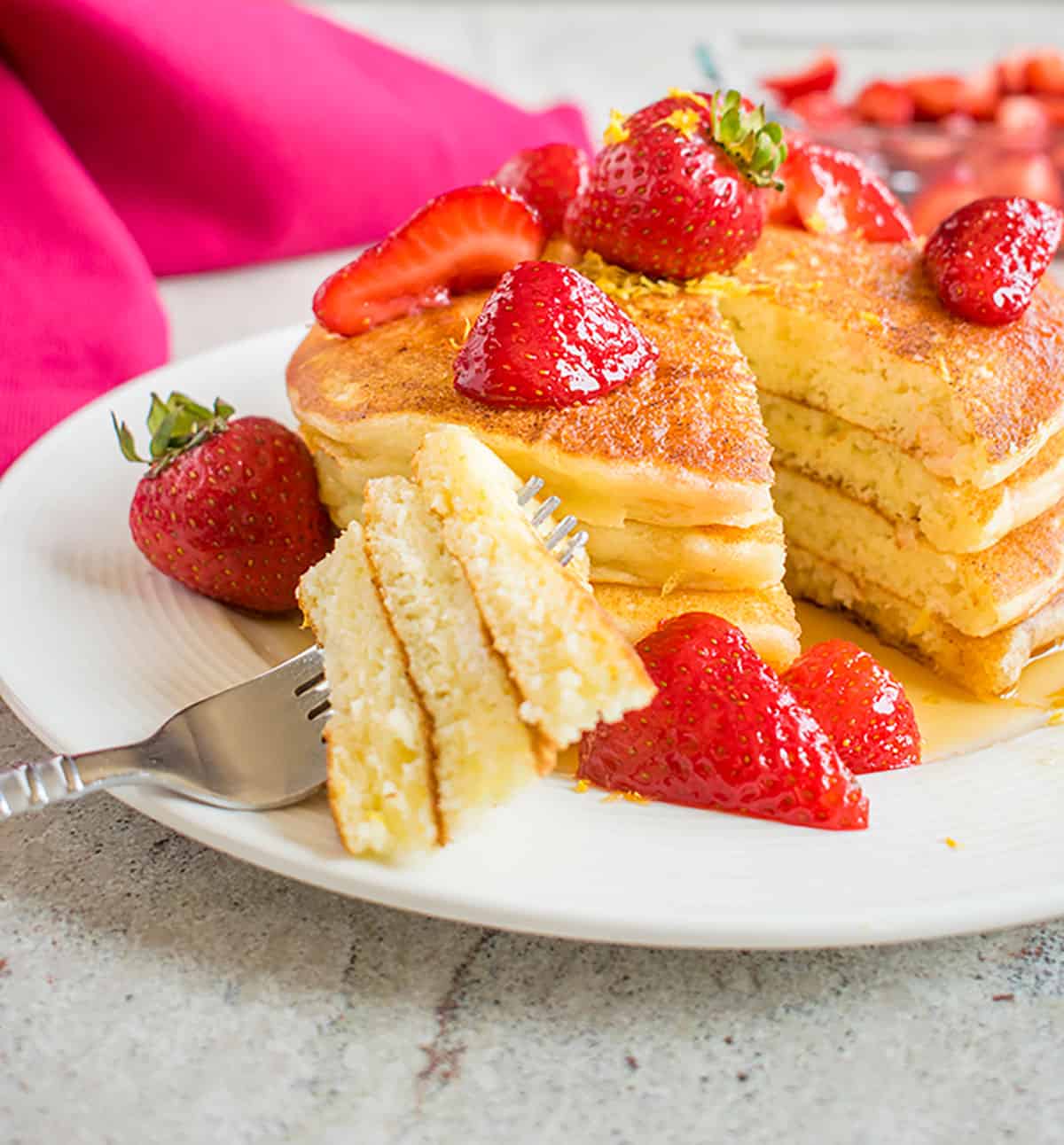 stack of lemon pancakes with strawberries and forkful of three pieces.