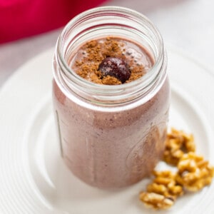 chocolate cherry smoothie in a mason jar on a plate with walnuts