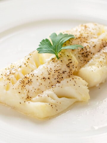baked cod on white plate with pepper and parsley