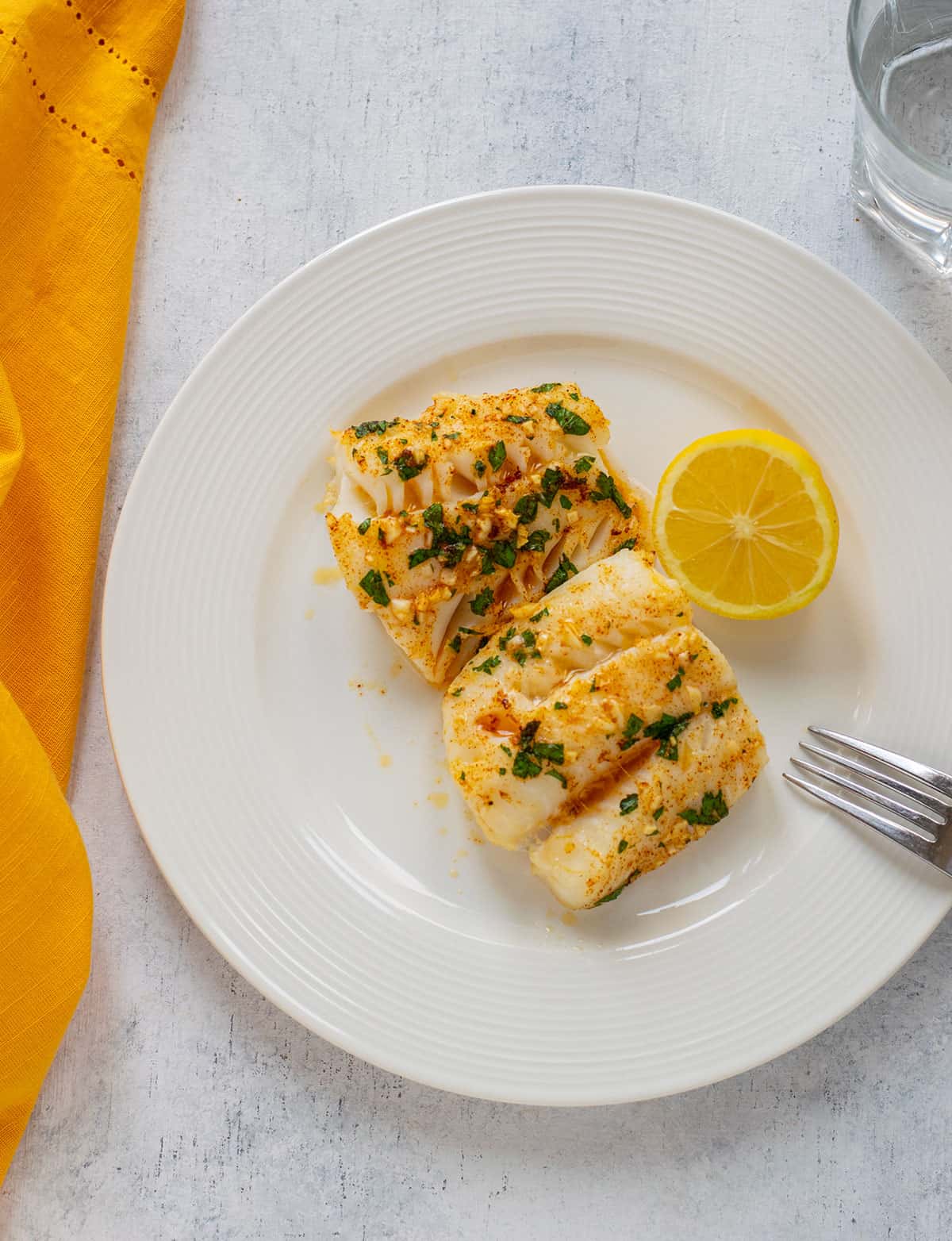 two pieces of garlic butter baked cod on a plate garnished with parsley