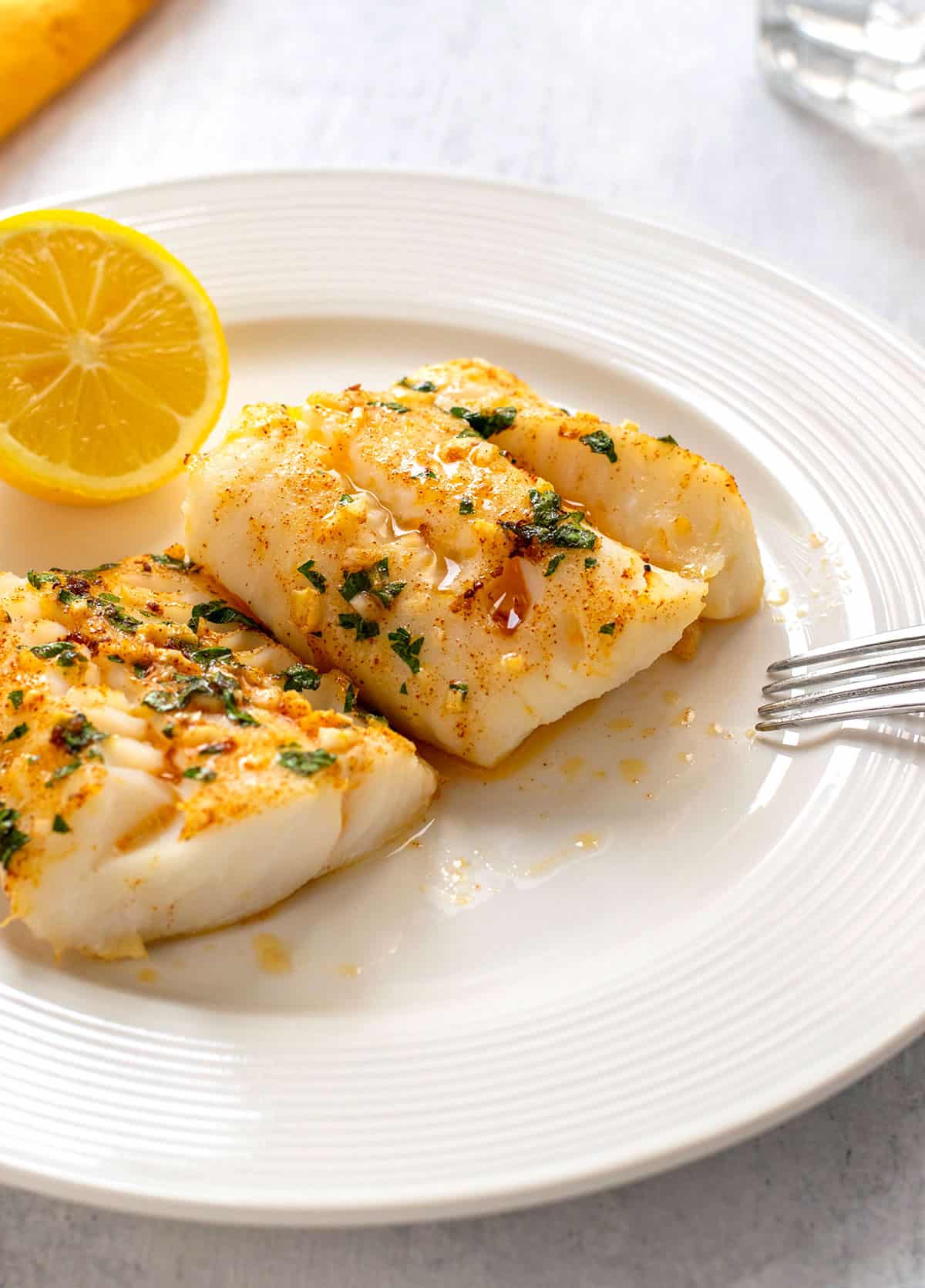 two pieces of garlic butter baked cod on a plate garnished with parsley