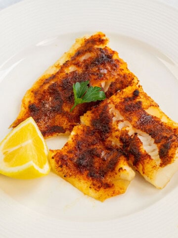 Plate of air fryer cod garnished with parsley and lemon wedge