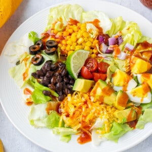 plate of salad with corn, olives, lime, cheese, avocado, tomatoes, onions, beans, eggs.