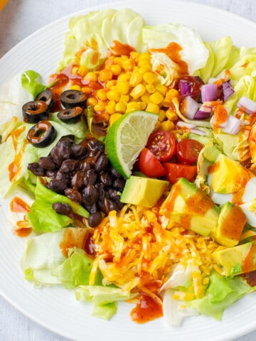 plate of salad with corn, olives, lime, cheese, avocado, tomatoes, onions, beans, eggs.