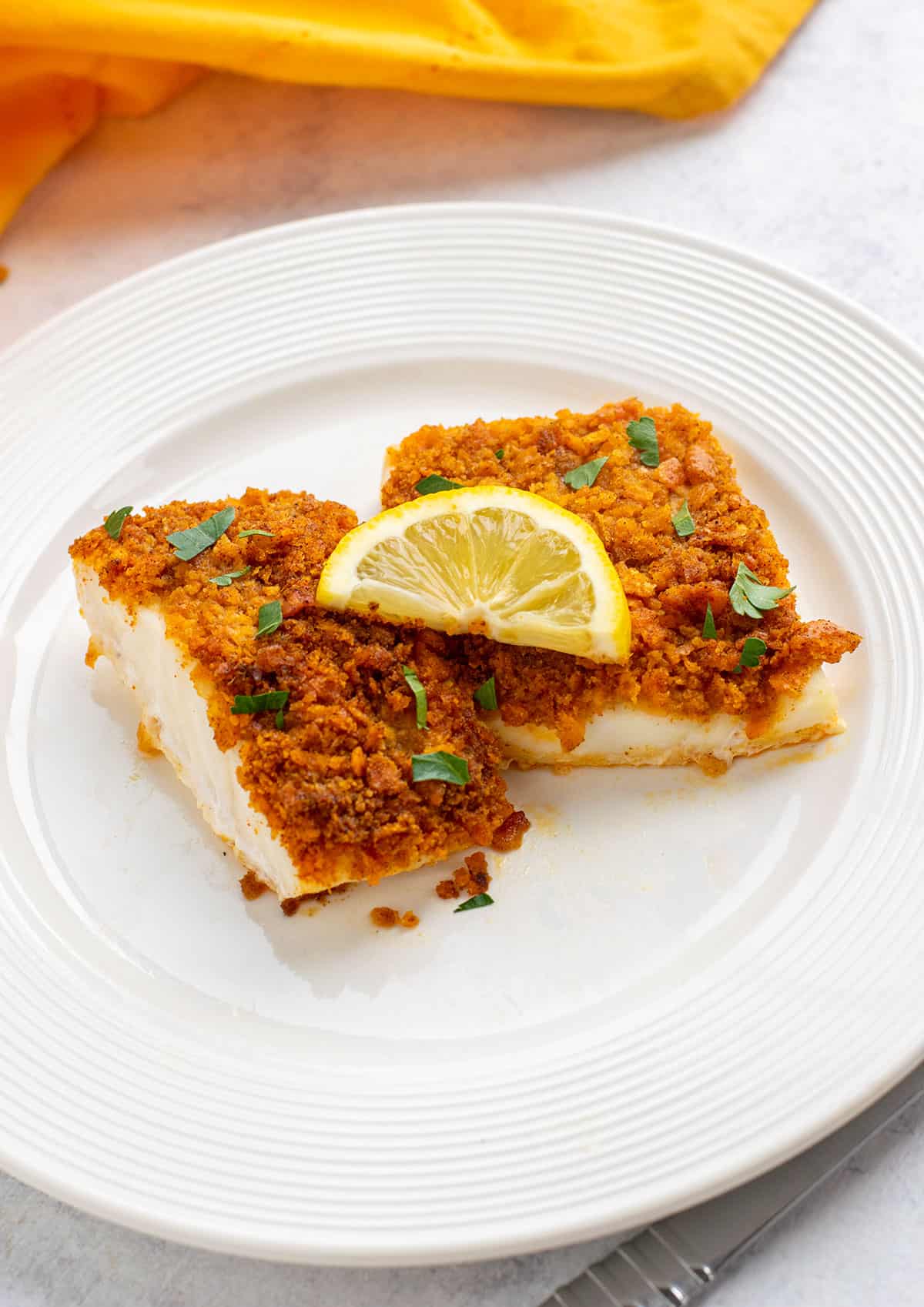plate of cracker crusted cod garnished with parsley and lemon slices