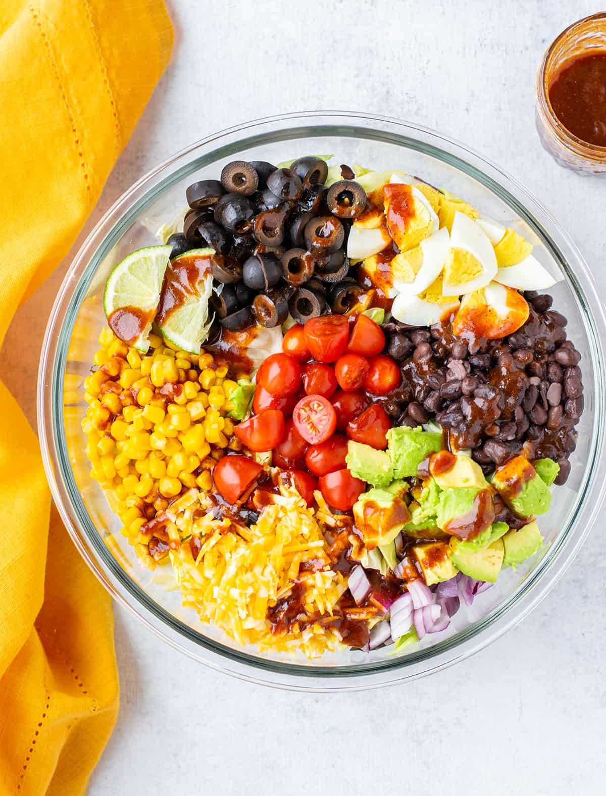 bowl of salad with corn, olives, lime, cheese, avocado, tomatoes, onions, beans, eggs.