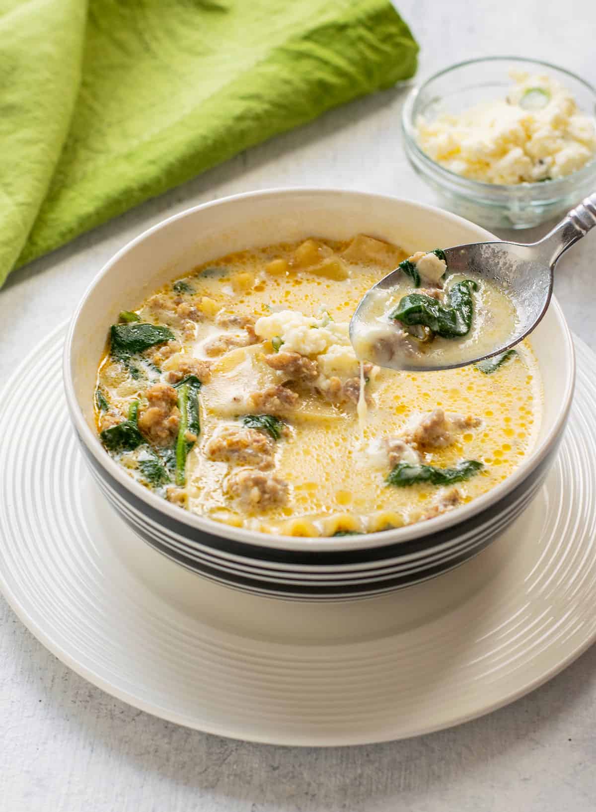 spoonful and bowl of white lasagna soup topped with ricotta