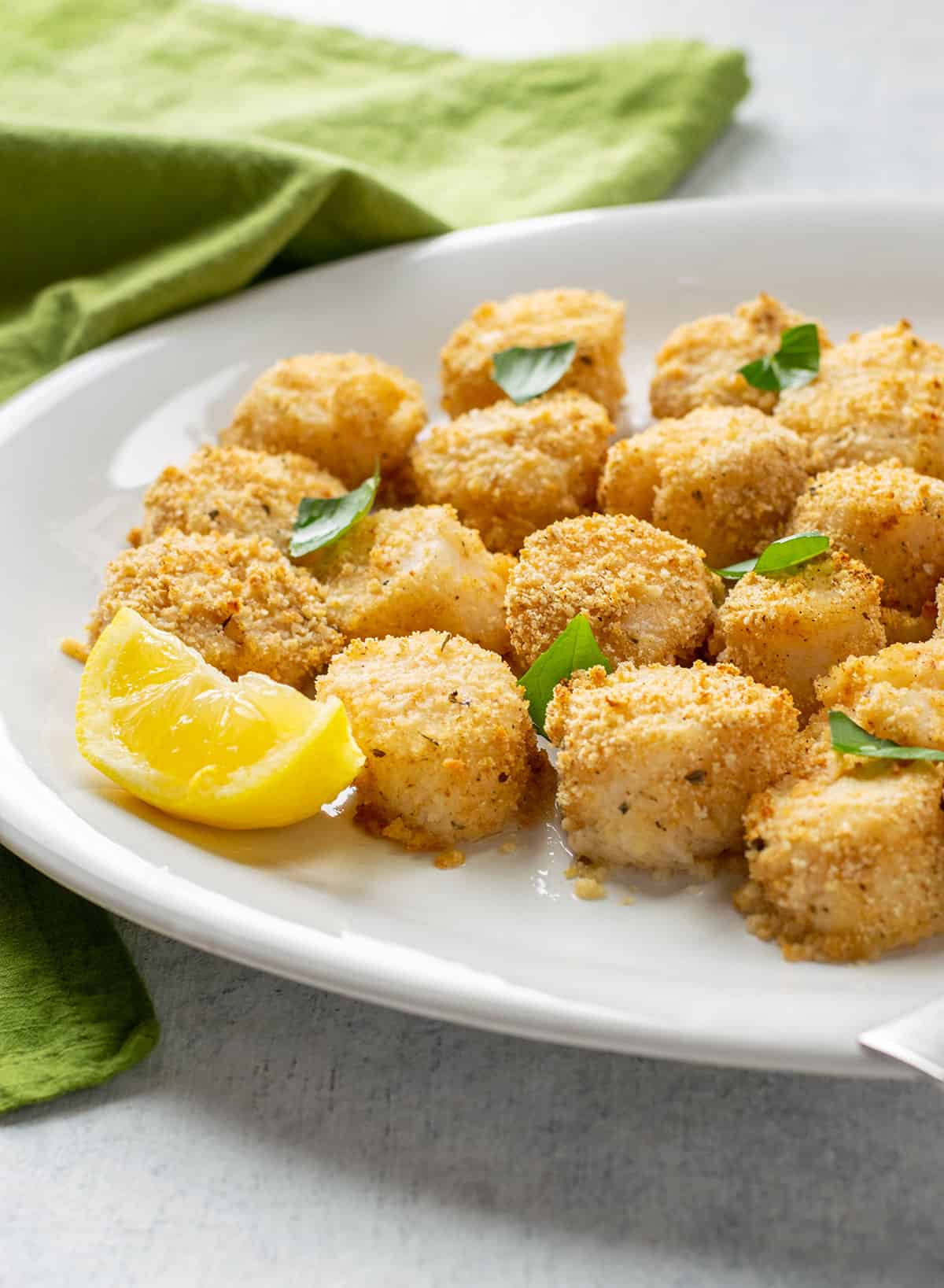platter of breaded sea scallops garnished with basil leaves and lemon