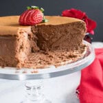 partially cut chocolate cheesecake on a cake stand with strawberries