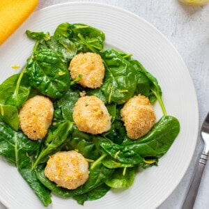 plate of spinach salad topped with breaded sea scallops