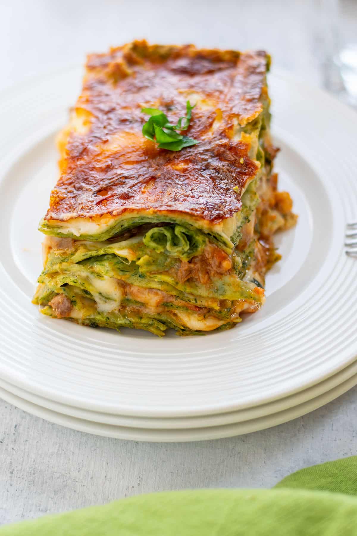 slice of lasagna bolognese on a plate with a fork and basil