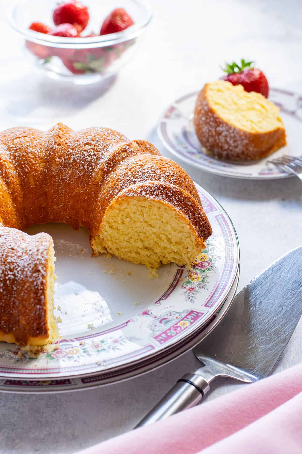 bundt cake cut on a dish with a slice and strawberries behind
