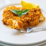 breaded cod on a plate with a fork-full and topped with basil