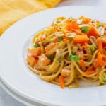 plate of pasta with peanut sauce, carrots, peppers, peanuts and green onion
