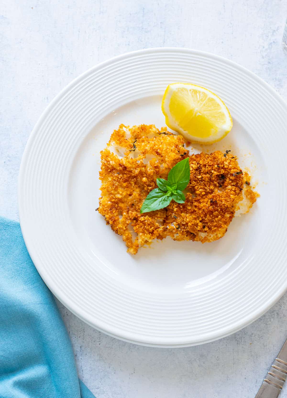 baked breaded cod on a plate with lemon topped with basil