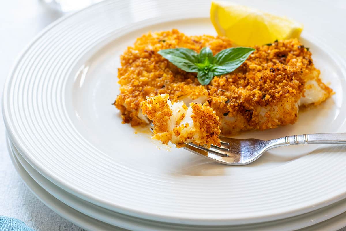 breaded cod on a plate with a fork-full and topped with basil