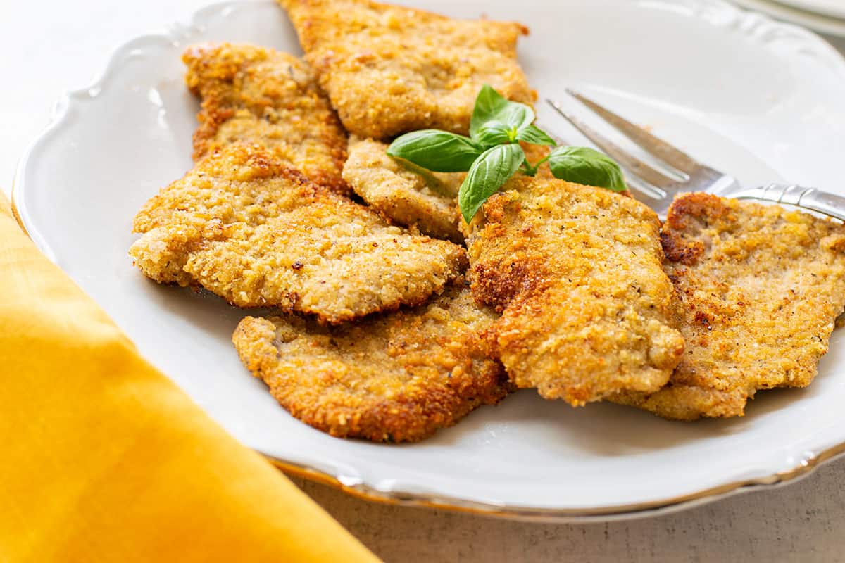 breaded veal cutlets on a plate topped with basil