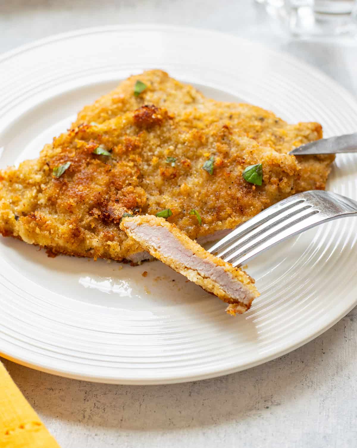 breaded veal cutlets on a plate topped with basil with a piece on a fork